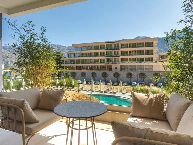 Terasa s posezením s výhledem na bazén a vícepodlažní hotelovou budovu pod jasnou oblohou.