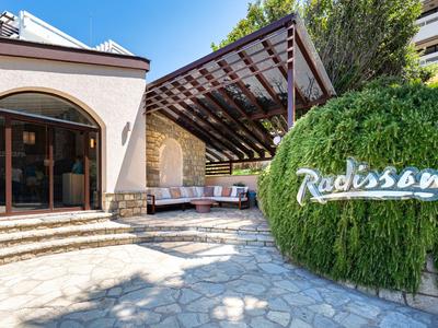 Venkovní prostor hotelu s krytým posezením a zeleným logem Radisson.