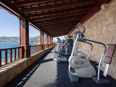 Fitness zařízení na venkovní terase s výhledem na moře a dřevěným zábradlím v hotelu.