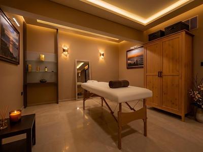Pohodlná wellness místnost s masážním stolem, teplým osvětlením a dřevěnou skříní pro relaxaci.