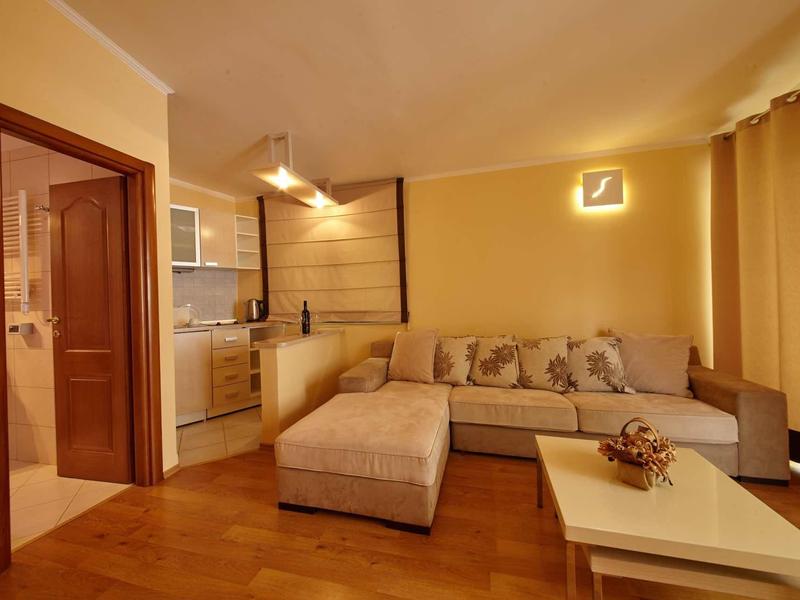 Cozy living room with corner sofa, coffee table, and open kitchen in warm lighting.