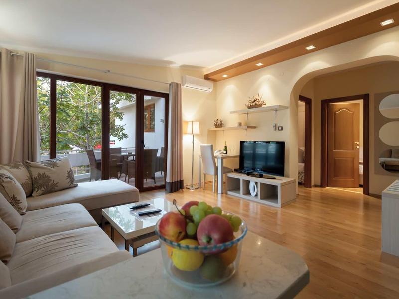 Bright living room with large sofa, TV, and balcony overlooking greenery.