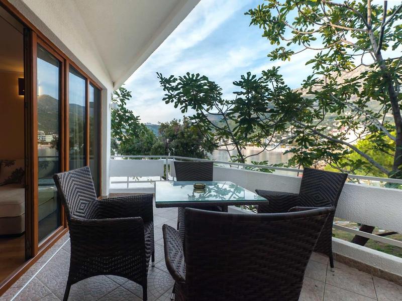 Balcony with glass table and four black chairs, surrounded by trees and view of buildings.