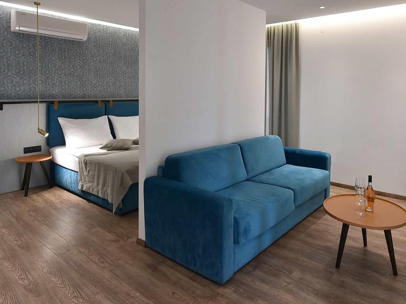 Modern hotel room with blue sofa, wooden floor, and double bed in the background.