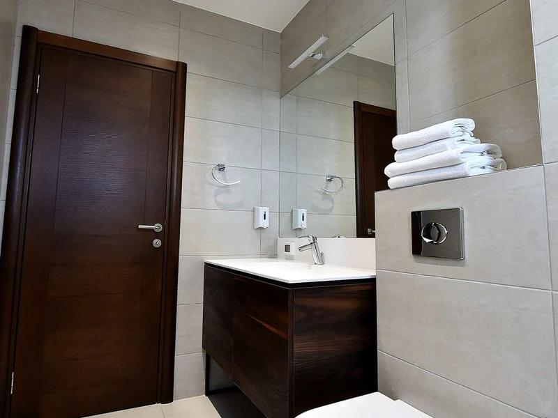 Modern bathroom with white toilet, dark vanity, and large light-colored tiles.