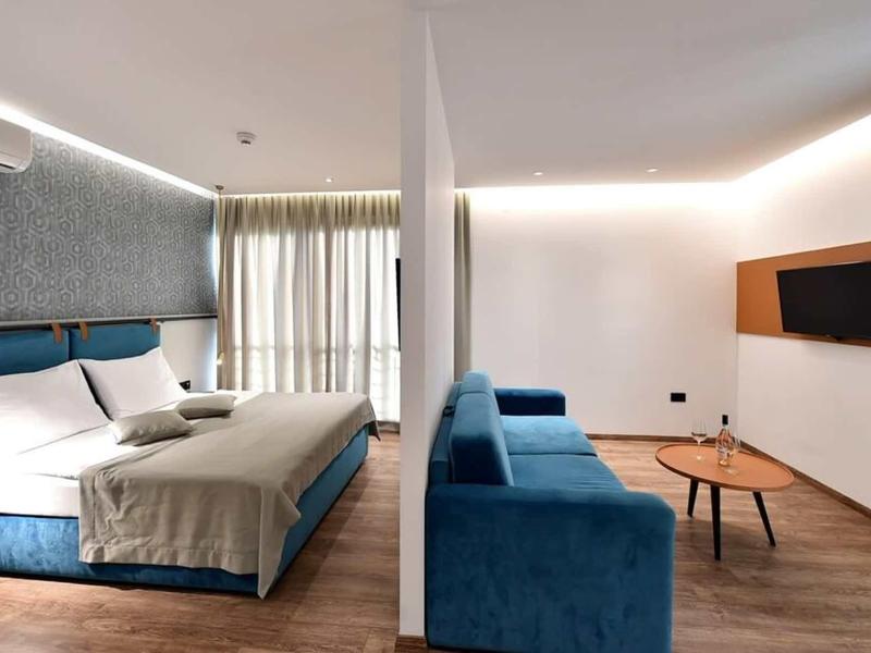 Modern hotel room with double bed, sofa, and flat-screen TV, bright atmosphere.