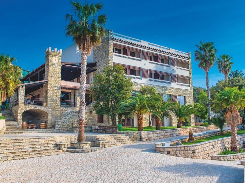 Hotel building with stone walls, palm trees, and clear blue sky in the background.