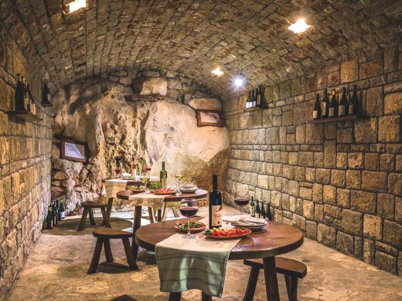 Cozy wine cellar with round wooden tables, benches, and stone walls.