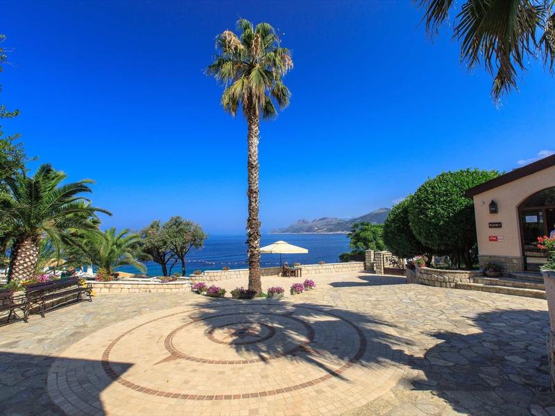 Seafront promenade with palm trees, sun umbrella, and clear blue sea under a bright sky.