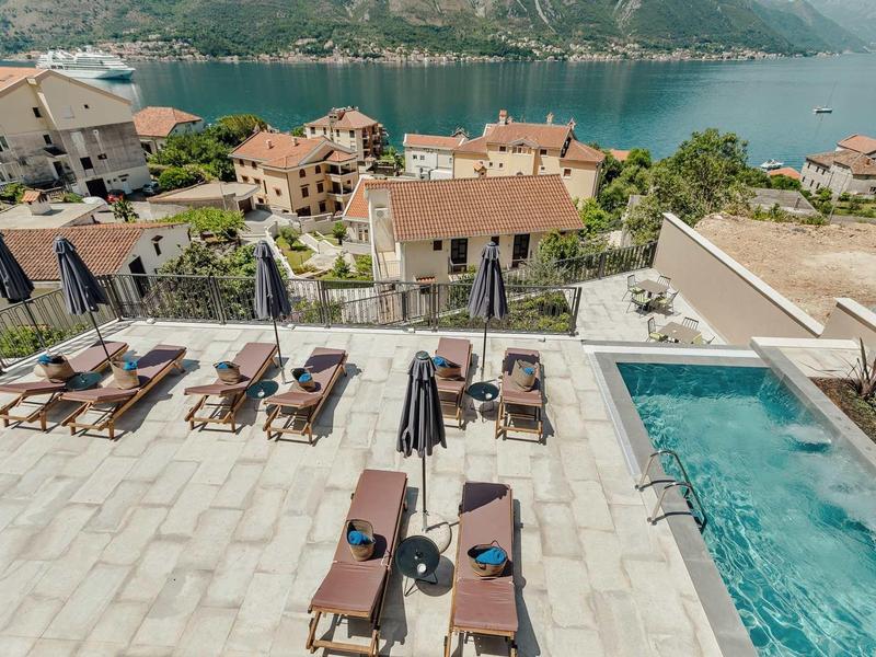 Terrasse avec chaises longues et piscine surplombant la baie et les montagnes en arrière-plan.