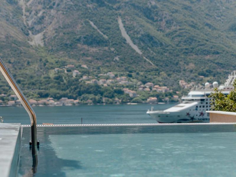 Piscine à débordement avec vue sur un lac et des montagnes, un grand bateau passe.