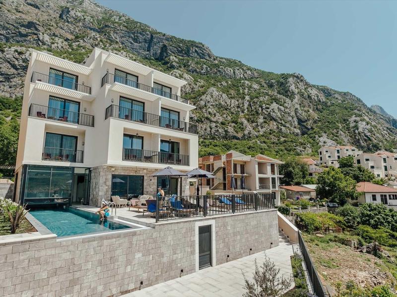 Bâtiment hôtelier moderne avec piscine devant un massif montagneux sous un ciel clair.