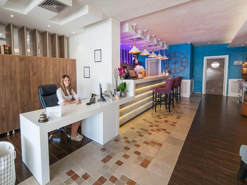 Área de recepción de hotel moderna con paredes claras, mostrador y asientos.