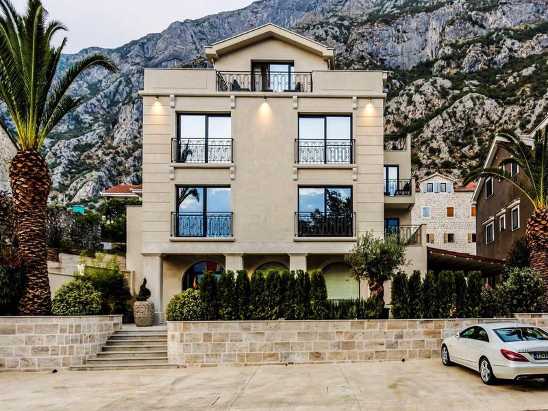 Mehrstöckiges Haus mit hellen Wänden, großen Fenstern, Palmen und Bergen im Hintergrund.