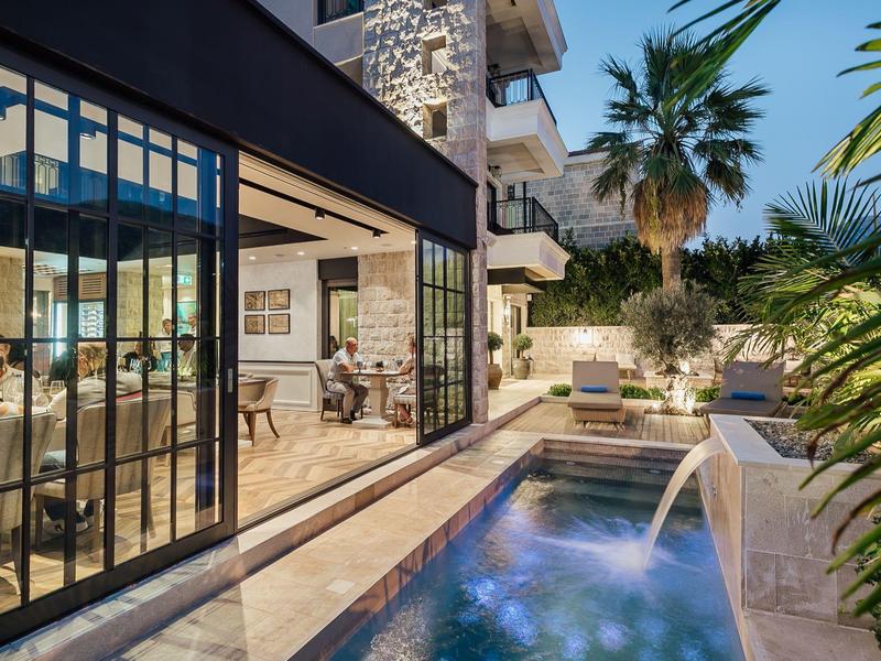 Modernes Haus mit großem Glasfenster, kleinem Pool und tropischen Pflanzen im Außenbereich.