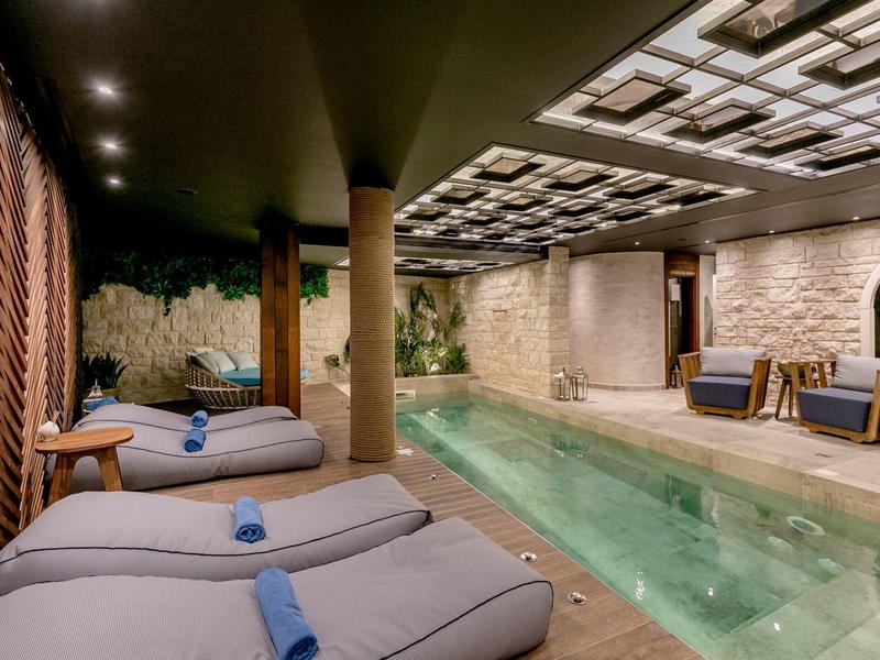 Innenpool mit Liegen, warmem Licht, Holzboden und offenem Deckenmuster in modernem Spa-Bereich.