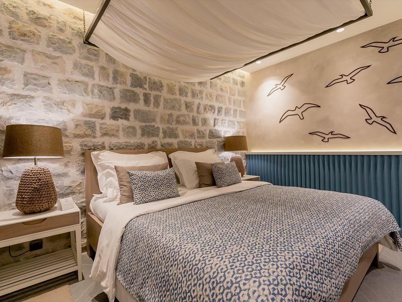 Gemütliches Schlafzimmer mit Steinwand, großem Bett, weichen Kissen und Vogelmotiven an der Wand.