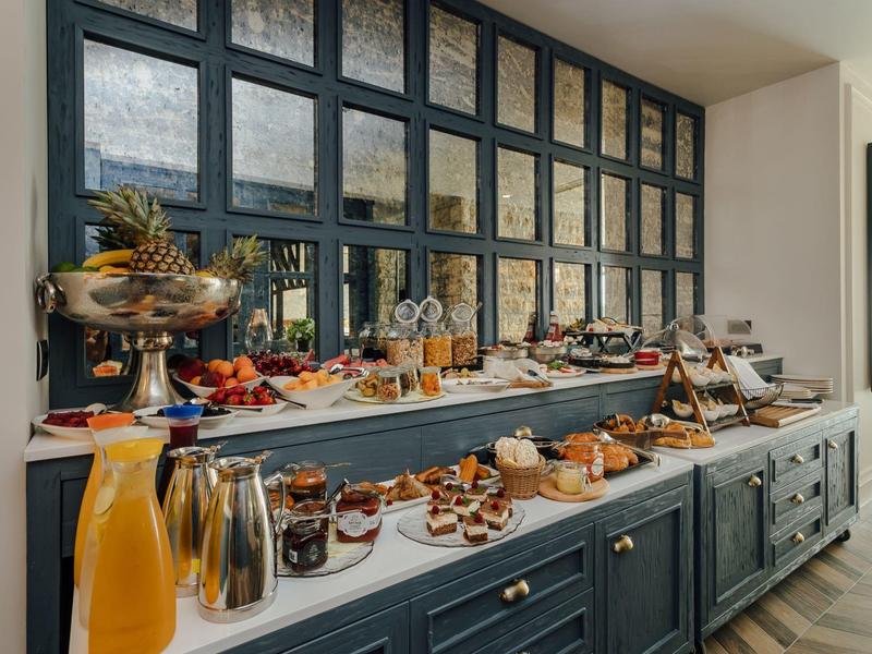 Buffet mit Obst, Säften, Brot und Aufstrichen auf dunkelblauen Schränken und großen Fenstern.