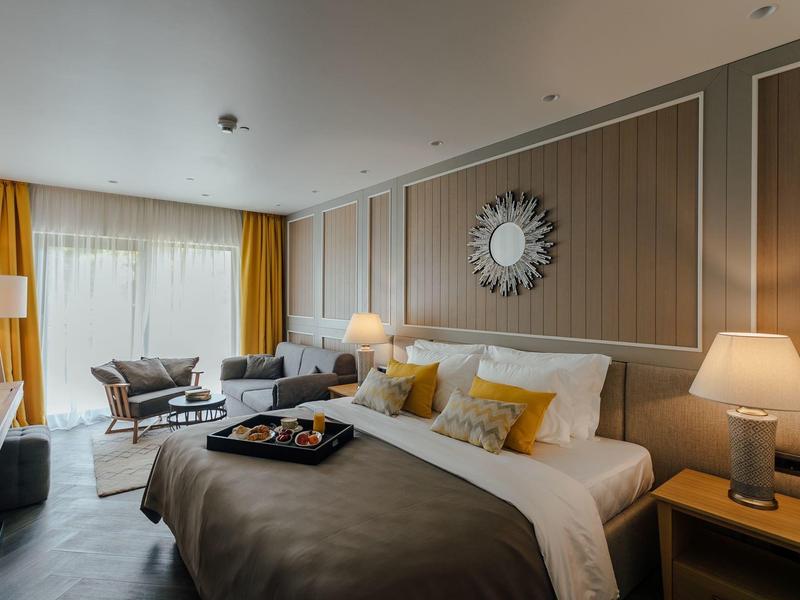 Modernes Schlafzimmer mit großem Bett, warmem Licht, gelben Vorhängen und gemütlicher Sitzecke.