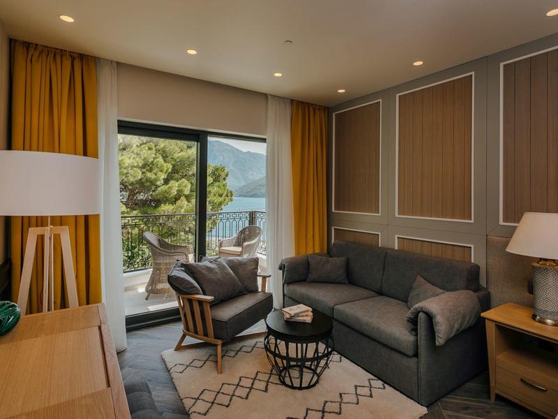 Modernes Wohnzimmer mit grauem Sofa, Sesseln, Teppich, Holzlampen und Blick auf Terrasse mit Meer.