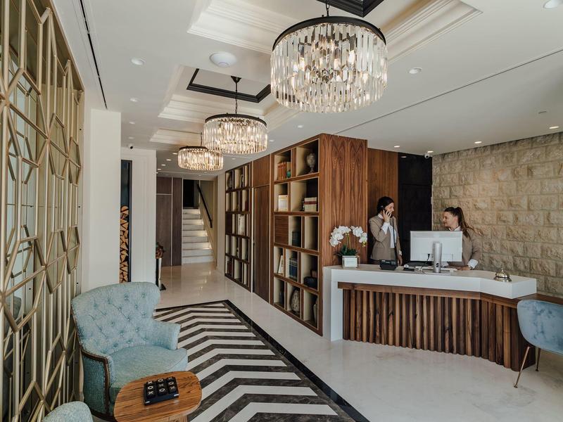 Hell eingerichteter Empfangsbereich mit Steinhintergrund, Holzregalen, blauen Sesseln und Kronleuchtern.