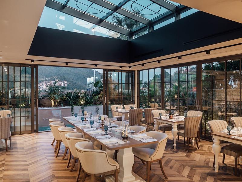 Helles Restaurant mit Glasdach, großen Fenstern, Holzboden und elegant gedeckten Tischen.