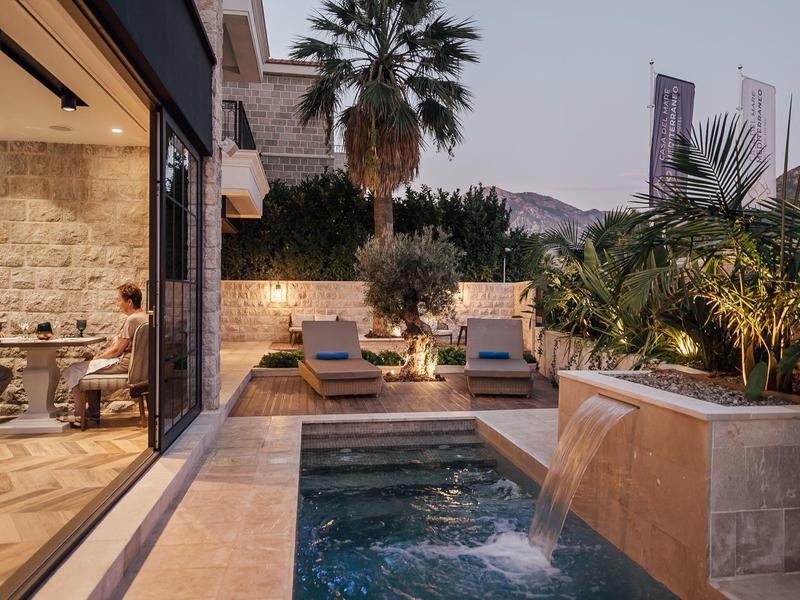 Moderner Garten mit kleinem Pool, Wasserfall, Liegestühlen und üppigen Palmen bei Dämmerung.