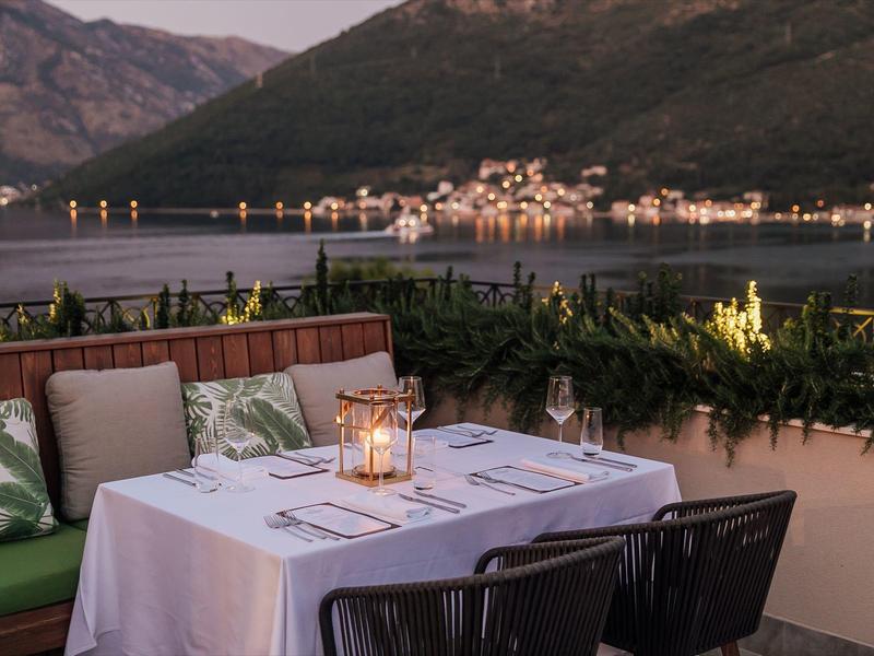 Romantischer gedeckter Tisch mit weißen Tischdecke und Kerzen auf Terrasse mit Berg- und Seenblick.