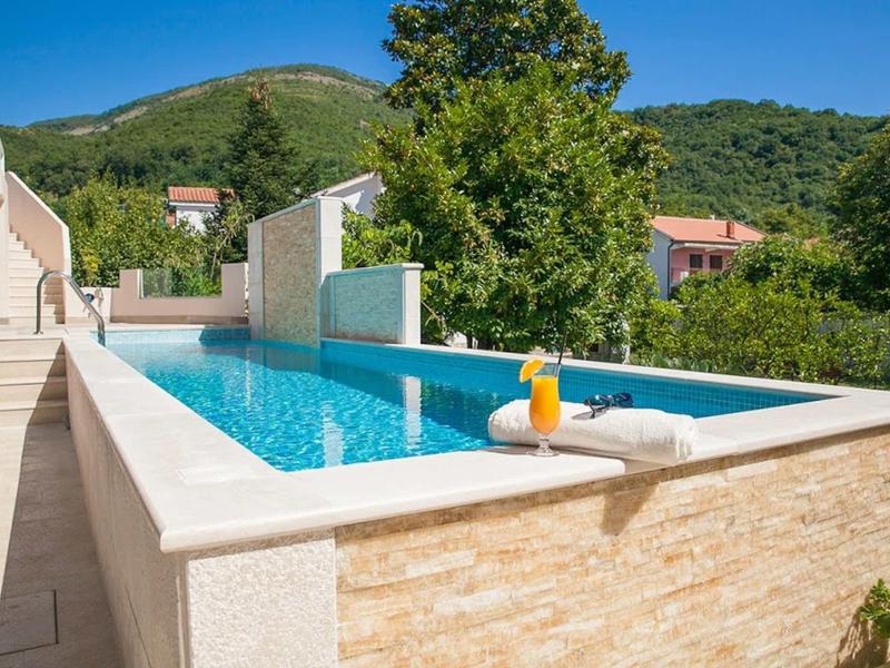 Ein langer Pool in einem Garten mit grünem Hügel im Hintergrund und einem Drink am Beckenrand.