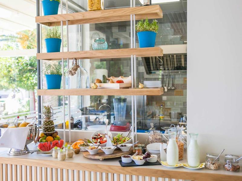 Buffet mit frischem Obst, Säften und Gebäck auf Holztisch vor Regalen mit blauen Blumentöpfen.