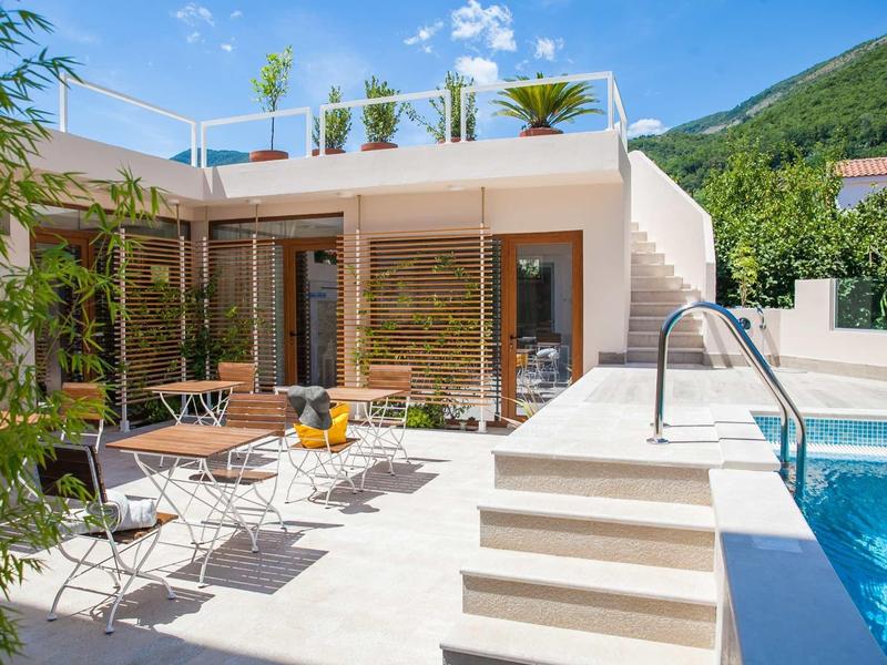 Moderner Garten mit weißem Haus, Terrasse, Pool und Metall-Gartenmöbeln bei sonnigem Wetter.