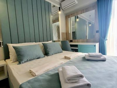 Modernes Hotelzimmer mit großem Bett, blauen Kissen und Tagesdecke, Fenster mit Vorhängen.