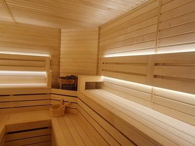 Helle Holzsauna mit mehrstufigen Sitzbänken und indirekter weißer LED-Beleuchtung entlang der Wände.