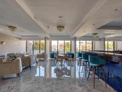 Heller, moderner Barbereich mit grünen Barhockern, beigen Sesseln und großen Fenstern mit Außensicht.