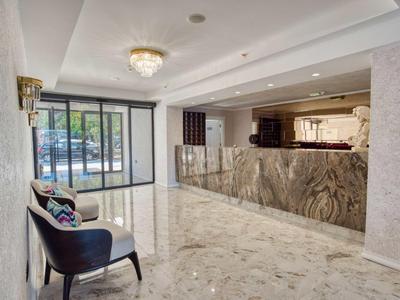 Heller Eingangsbereich mit Marmorboden, dunklem Sessel, dekorativem Tresen und großer Glasschiebetür.