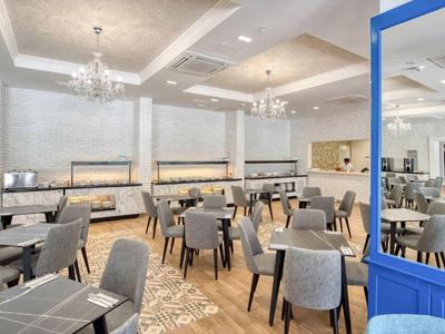 Moderner, heller Gastraum mit grauen Stühlen, Holzboden und großer blauer Glastür.