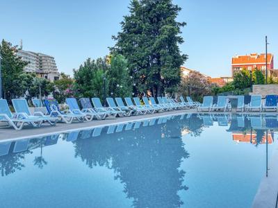 Piscina vuota con lettini bianchi e alberi sullo sfondo sotto un cielo limpido.