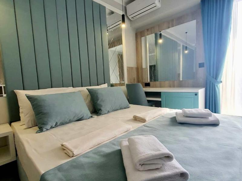 Modernes Hotelzimmer mit großem Bett, blauen Kissen und Tagesdecke, Fenster mit Vorhängen.