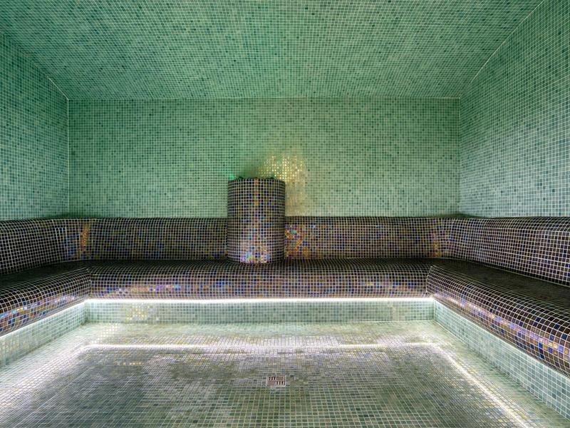 Leerer Innenpool mit grünen und braunen Fliesen, rechteckig und von Wänden umgeben.