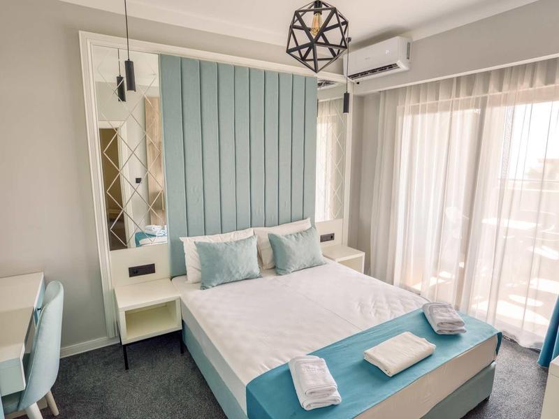 Helles Schlafzimmer mit Doppelbett, blauen Akzenten, Spiegelwand und großen Fenstern mit Vorhängen.