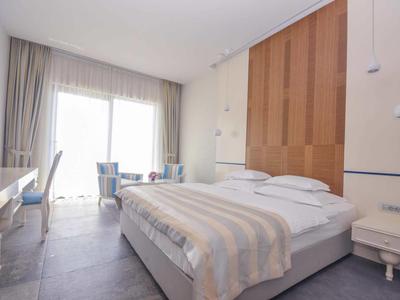 Helles Schlafzimmer mit großem Bett, Holzwand, Schreibtisch und bodentiefen Fenstern.