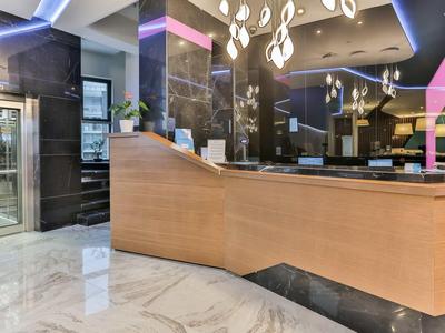 Moderní recepce hotelové haly se světlým dřevem, mramorovou podlahou a stylovým osvětlením.