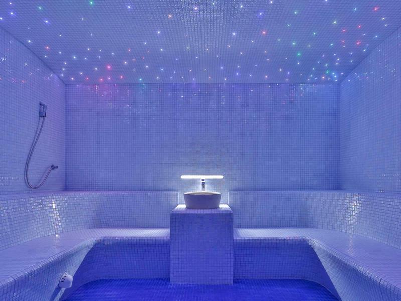 Hellblaue Dampfbadkabine mit Mosaikfliesen und Sternenhimmelbeleuchtung an Decke und Wänden.