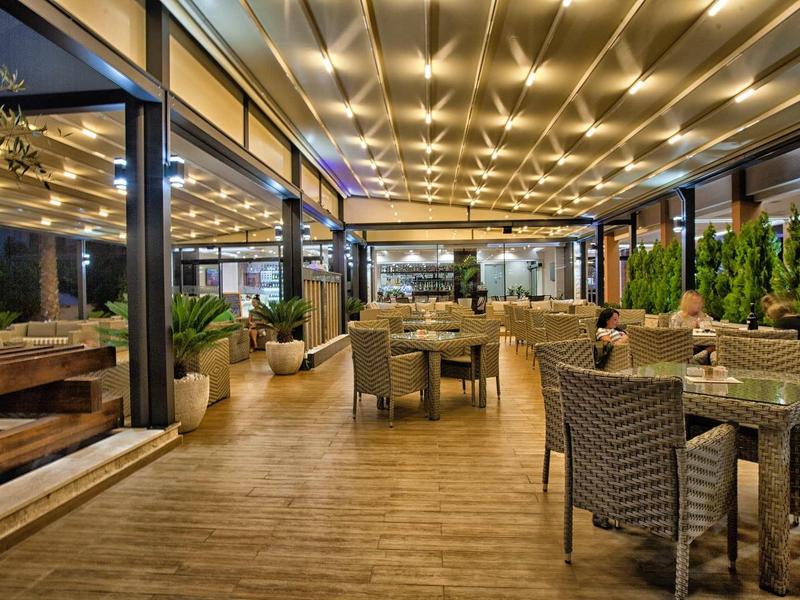 Moderner Außenbereich eines Restaurants mit Holzfußboden, beleuchteten Decken und gepolsterten Stühlen.