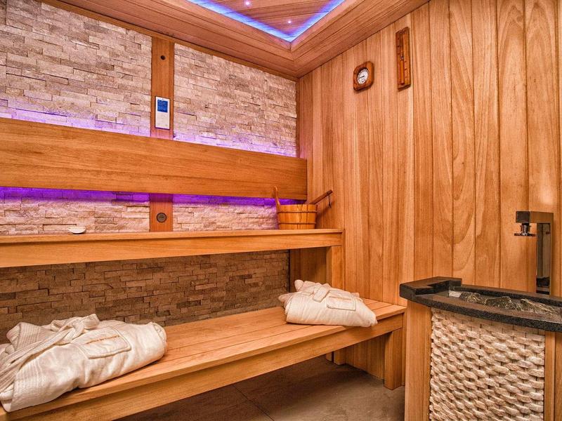 Gemütliche Sauna mit Holzvertäfelung, Steinwand, Bank, Beleuchtung und Handtüchern.
