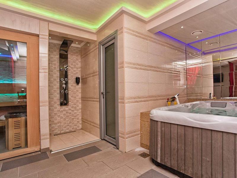 Moderner Wellnessbereich mit Sauna, Dusche, Whirlpool und indirekter LED-Beleuchtung in Holz- und Fliesendesign.