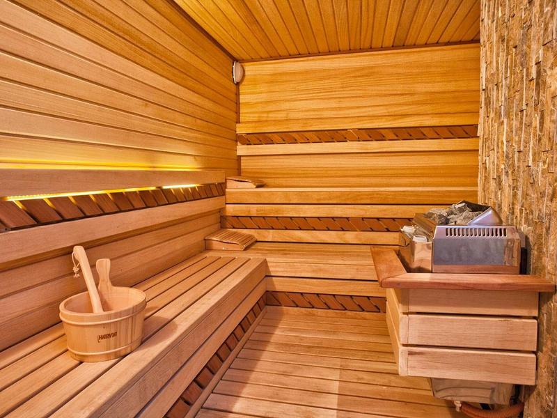 Holzsauna mit mehrstufigen Sitzbänken, Saunaofen, Holzeimer und warmem Licht.