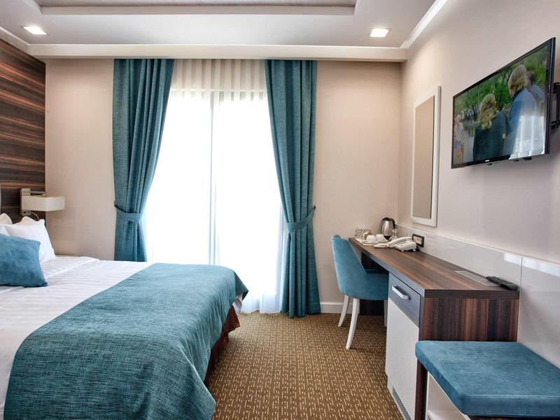 Modernes Schlafzimmer mit großem Bett, türkisfarbenen Vorhängen und Holzmöbeln.