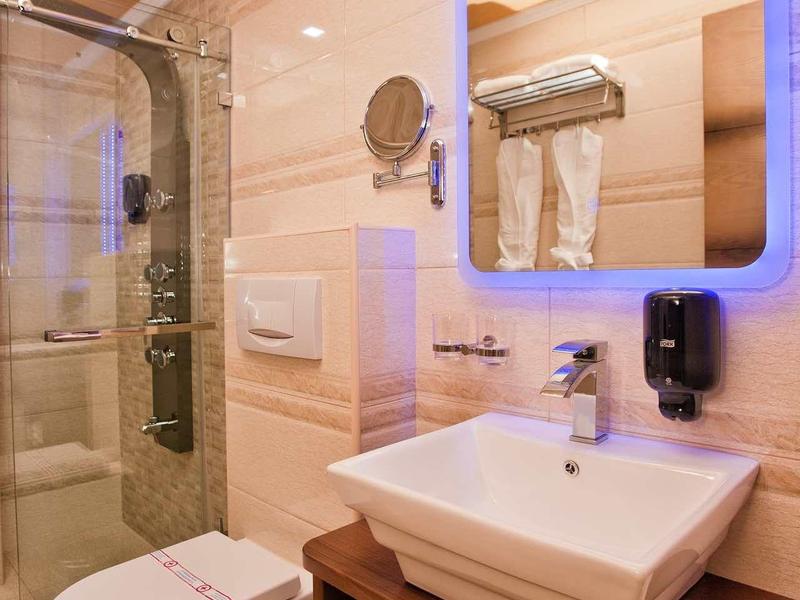 Modernes Badezimmer mit Glasdusche, beleuchtetem Spiegel und weißem Waschbecken auf Holzablage.