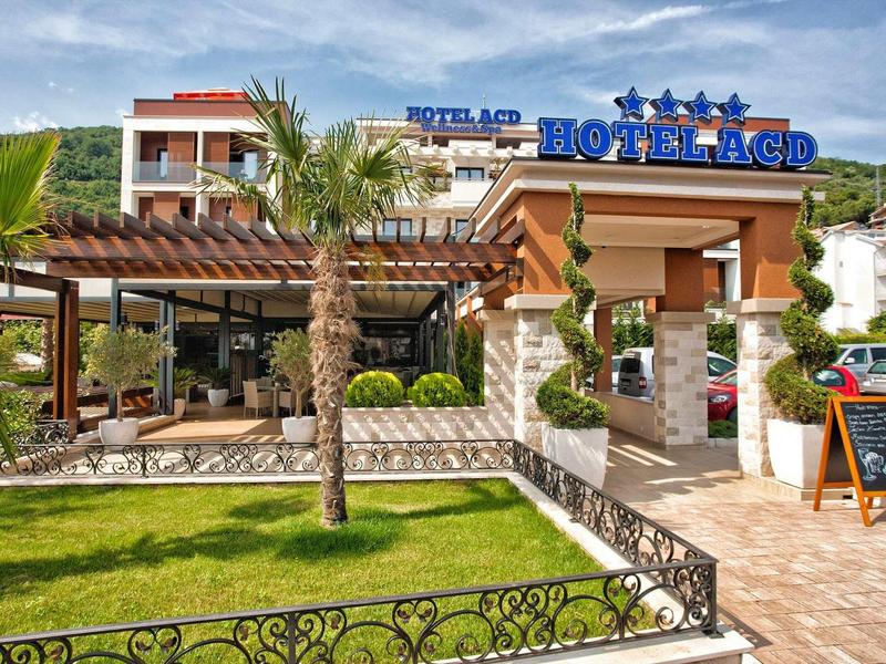 Hotelgebäude mit Terrasse, Palmen und grünem Garten unter blauem Himmel.